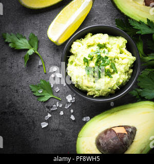 Latinoamericana tradizionale salsa messicana guacamole in una ciotola di ardesia scuro dello sfondo. Vista dall'alto uno spazio di copia. Square. Foto Stock