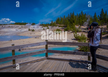 YELLOWSTONE, Montana, USA Giugno 02, 2018: donna non identificato a scattare foto e godere della vista delle piscine di colorfully acqua colorata dot del Norris Geyser Basin nel Parco Nazionale di Yellowstone Foto Stock