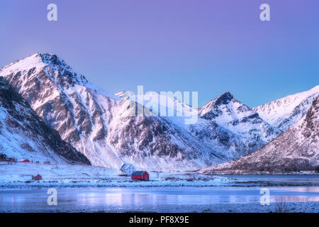 Case e belle montagne coperte di neve in inverno al tramonto. Bellissimo fiordo e piccolo villaggio di notte nelle Isole Lofoten in Norvegia. Paesaggio nordico Foto Stock