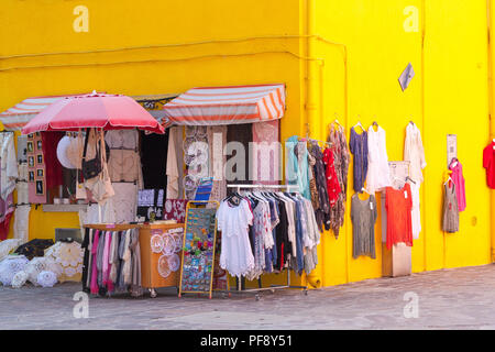 Tramonto nel colorato villaggio di pescatori sull'isola di Burano, Venezia, Veneto, Italia. Giallo luminoso negozio con display di vestiti, i merletti di Burano e negozio di souvenir Foto Stock