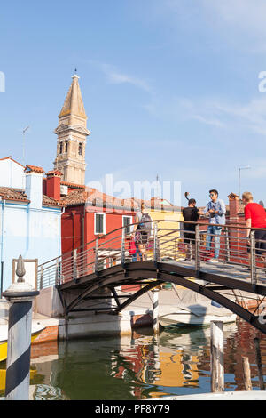 Tramonto nel colorato villaggio di pescatori sull'isola di Burano, Venezia, Veneto, Italia, turisti sul ponte prendendo selfies, riflessioni canal, pendente a campana Foto Stock