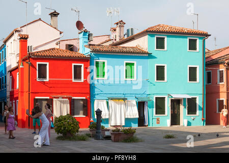 Tramonto nel colorato villaggio di pescatori sull'isola di Burano, Venezia, Veneto, Italia. Luminose colorate case, persone Scattare foto nella piccola piazza con wa Foto Stock