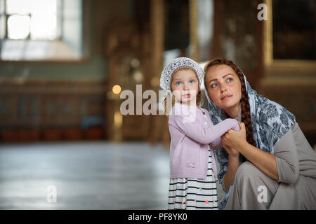 Giovane madre e la sua piccola bionda figlia caucasici con candele in ortodossi Chiesa Russa Foto Stock
