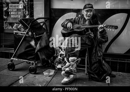 Senzatetto musicista di strada in strada con averi nel centro della città di Manchester, Inghilterra, Regno Unito Foto Stock