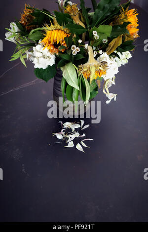 Guardando leggermente verso il basso in corrispondenza di un vaso di morire floreale, grande una volta ora brillante sole morente fiori in un vaso su un grande tavolo da pranzo è in marmo Foto Stock