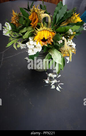 Guardando leggermente verso il basso in corrispondenza di un vaso di morire floreale, grande una volta ora brillante sole morente fiori in un vaso su un grande tavolo da pranzo è in marmo Foto Stock