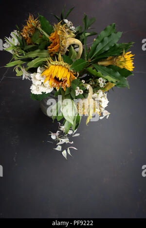 Guardando leggermente verso il basso in corrispondenza di un vaso di morire floreale, grande una volta ora brillante sole morente fiori in un vaso su un grande tavolo da pranzo è in marmo Foto Stock