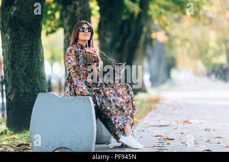 Giovane donna in occhiali da sole con il frullato. Outdoor Lifestyle ritratto di bella donna sorridente con piccolo cucciolo in autunno park Foto Stock