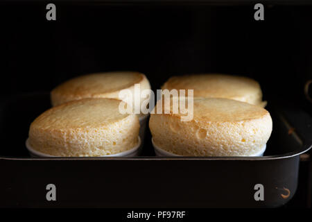 Quattro soufflé in ceramica bianca vaso (ramekin) su forno, fatti in casa Foto Stock