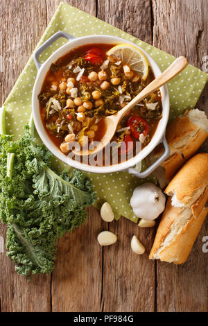 Zuppa di ceci, kale, pomodori, aglio e patate con limone vicino fino in una ciotola sul tavolo. Verticale in alto vista da sopra Foto Stock