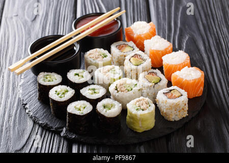 Rotoli di Sushi set con salse servito su nero ardesia pietra su sfondo scuro. Posizione orizzontale Foto Stock