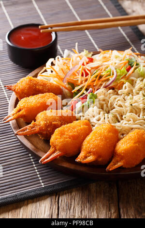 Fritte chele di granchio in una panatura, udon noodles e fresca insalata di verdure close-up su una piastra su un piano verticale. Foto Stock