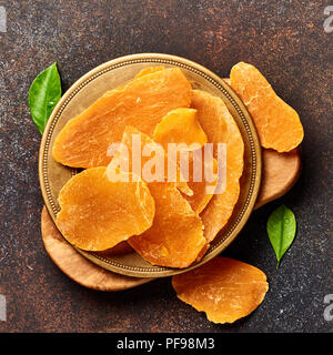 Mango essiccato fette. Vista superiore della frutta candita su sfondo marrone. Foto Stock