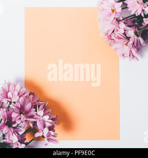 Modello di cartolina decorate con freschi fiori lilla crisantemi negli angoli. Verticali arancioni foglio di carta tra il piatto floreale telaio laici. Foto Stock