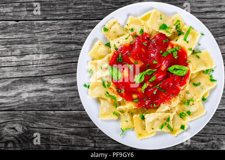 Italian ravioli ripieni di ricotta e spinaci con salsa di pomodoro e le foglie di basilico cosparsi di pepe nero macinato fresco su un piatto bianco o Foto Stock