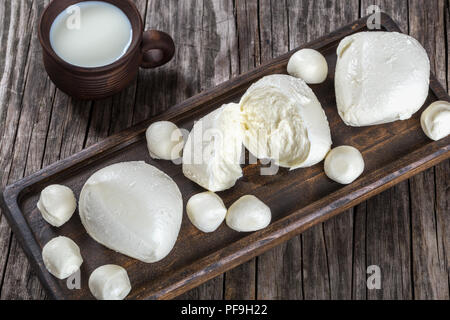 Le sfere di mozzarella al buio su un bordo e tazza di argilla con il latte su un vecchio tavolo rustico, vista dall'alto Foto Stock