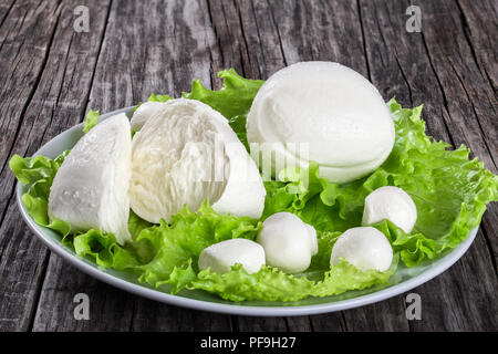 Le sfere di mozzarella e le foglie di lattuga sul piatto di portata su un vecchio tavolo rustico, close-up Foto Stock