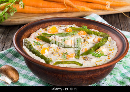 Delizioso formaggio cremosa zuppa di funghi con molla carote, gli asparagi e le spezie, decorata con aneto, in un vaso di argilla su un vecchio tavolo rustico, horizonta Foto Stock