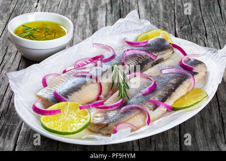 Filetti di aringhe con cipolla e fettine di lime su carta pergamena su un ovale piatto su un vecchio tavolo rustico, close-up Foto Stock