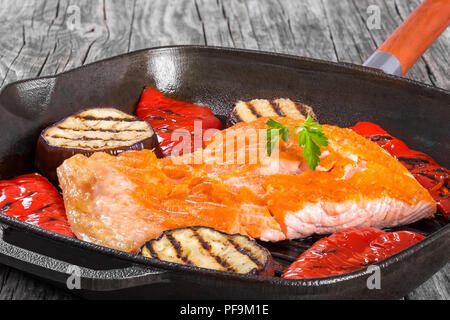 Delizioso pesce rosso salmone filetto di bistecca su un ferro padella per grigliare con grigliate di peperone e grigliate di fette di melanzana, luci dello studio, close-up Foto Stock