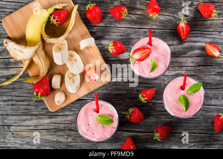 Fragola Banana Smoothies Cups , fette di banana su un bordo di taglio su una vecchia tavola in legno rustico, luci dello studio, vista da sopra Foto Stock