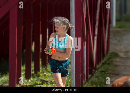 Estate in un momento di divertimento, di bambini e adulti utilizzando secchi, squirt pistole e soakers, in una lotta di acqua. Sorridente bionda con pistola ad acqua, ridendo. Modello rilasciato, Foto Stock