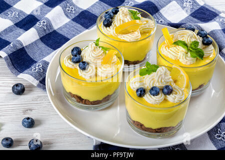 Layered sana colazione - Limone dessert di mirtilli in bicchieri di vetro decorate con panna montata su piastra bianca, le fette di limone e menta con cucina towe Foto Stock