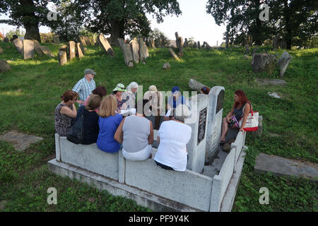 I partecipanti dell'agenzia di tour ROOTKA specializzata in tour del patrimonio ebraico nell'Europa orientale siedono tra vecchie lapidi nel cimitero ebraico abbandonato contenente quasi 3000 lapidi nei sobborghi di Bolekhiv una città regionale di Ivano-Frankivsk Oblast (provincia) dell'Ucraina, che un tempo ospitava una grande comunità ebraica. Durante l'Olocausto, la comunità ebraica è stata annientata, brutalmente, dai tedeschi con i collaboratori ucraini locali. Foto Stock