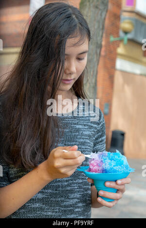 Inglese/Thai ragazza adolescente con lunghi capelli neri mangia una granita blu nel centro citta' di Warrington Foto Stock