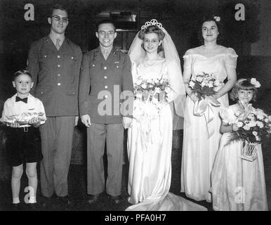 Fotografia in bianco e nero, mostrando un groom in uniforme militare e bicchieri, in piedi accanto ad una sposa che indossa un abito bianco, velo, tiara e bicchieri, fiancheggiata da il miglior uomo (anche in uniforme) e un giovane portatore ad anello sulla sinistra e la cameriera di onore e un giovane damigella (entrambi holding fiori) sulla destra, fotografato in Ohio, 1945. () Foto Stock