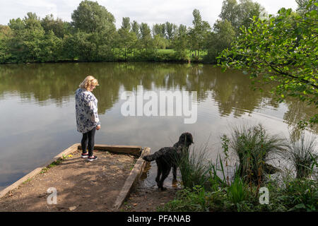 Coppia bionda signora sorge sul lato del lago a tre sorelle natura locale riserva, tre sorelle Road, Ashton-In-Makerfield, Wigan con il suo nero Foto Stock