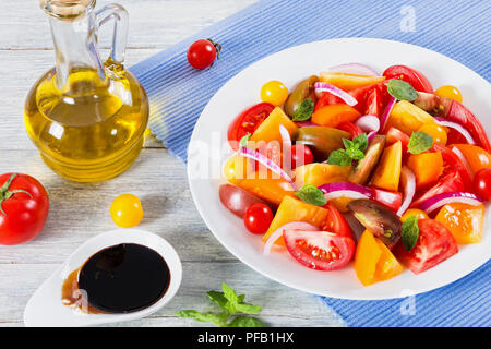 Insalata di pomodoro con cipolla rossa, foglie di menta e olio d'oliva sul piatto bianco, close-up Foto Stock