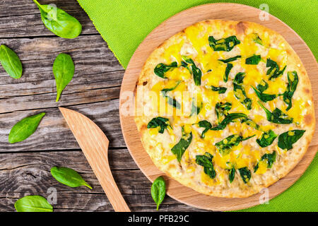 Deliziosa casa spinaci formaggio sulla pizza tonda in legno tagliere con coltello in legno sul vecchio tavolo rustico,vista da sopra, close-up Foto Stock