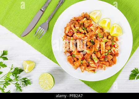 Brasato di orecchie di maiale o Oreja de cerdo decorate con il prezzemolo sul piatto bianco con spezie, peperoncino, fettine di lime sul tabella MAT, sul vecchio legno schede, Foto Stock