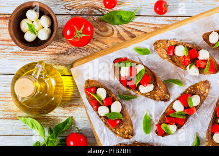 Bruschetta con pomodori, mini mozzarella e basilico sul fritto in olio di oliva della segala baguette con semi, bottiglia con olio, pomodoro e mozzarella in piccoli b Foto Stock