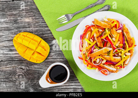 Mango, pane impanati Pollo, arachidi, il peperone e la cipolla rossa insalata sul piatto bianco con metà del mango tagliare a cubetti, aceto balsamico dressin Foto Stock