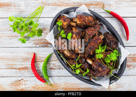 Delizioso caldo nervature appiccicosa condito con una piccante aglio zenzero salsa barbecue amd coriandolo ovale in teglia su bianco plance. verde e peperoncino rosso pe Foto Stock