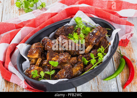 Delizioso caldo nervature appiccicosa condito con una piccante aglio zenzero salsa barbecue e coriandolo ovale in teglia su tavole di colore bianco con un panno da cucina. gre Foto Stock