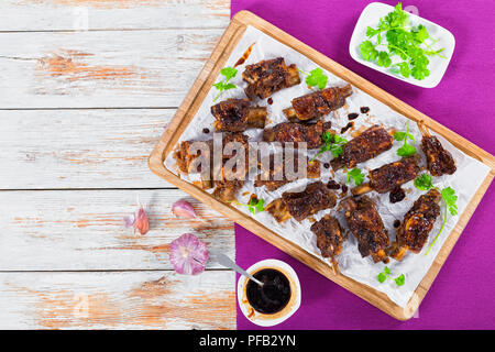 Delizioso caldo nervature appiccicosa condito con una piccante aglio zenzero salsa barbecue e coriandolo su carta pergamena sul tagliere. sulla tabella mat su bianco Foto Stock