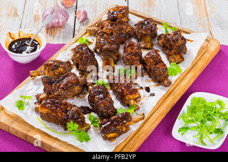 Delizioso caldo nervature appiccicosa condito con soia piccante aglio zenzero salsa barbecue sulla carta pergamena sul tagliere. sulla tabella MAT, close-up, visualizzare fro Foto Stock