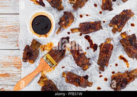 Delizioso caldo nervature appiccicosa condito con soia piccante aglio zenzero salsa barbecue su carta pergamena con una spazzola in legno tinta peeling background, visualizzazione Foto Stock