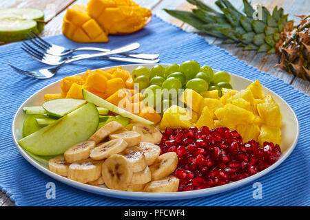 Deliziosa insalata di frutta con banana e mela verde fette, pezzetti di mango e ananas, uva, semi di melograno stabiliti sui segmenti su plat Foto Stock