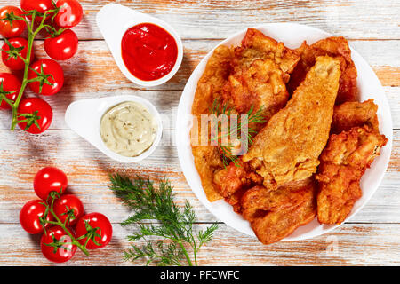 Deliziosa coppa croccante fritti martoriato di birra i filetti di pesce sulla piastra bianca sul vecchio tavolo in legno. ketchup e salsa tartara in salsa di barche, aneto e ciliegia tom Foto Stock