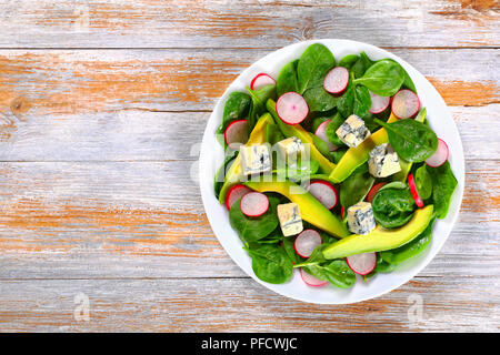 Fette di avocado, Formaggi a Muffa Blu, spinaci, molla il Ravanello di dieta sana insalata sul piatto bianco su assi di legno vista da sopra Foto Stock