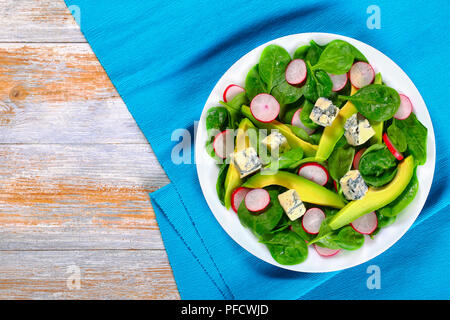 Fette di avocado, Formaggi a Muffa Blu, spinaci, molla il Ravanello di dieta sana insalata sul piatto bianco sulla tabella mat su assi di legno vista da sopra Foto Stock