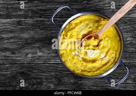 Hot deliziosa polenta porridge con il burro in padella con il cucchiaio di legno scuro sul piano di lavoro in legno, italiana autentica ricetta base, vista da sopra Foto Stock