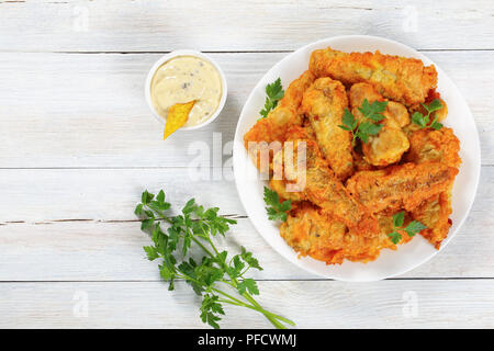 Golden delicious pastella pesce fritto decorate con prezzemolo e servite sulla piastra bianca con tartara di casalinghe saucein salsiera sul piano di lavoro in legno, vista dal Foto Stock