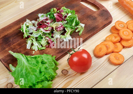 La cucina vegetariana concetto. Pronti a fare di insalata.un tagliere, coltello, spezie e verdure su un tavolo da cucina, vista dall'alto. Foto Stock
