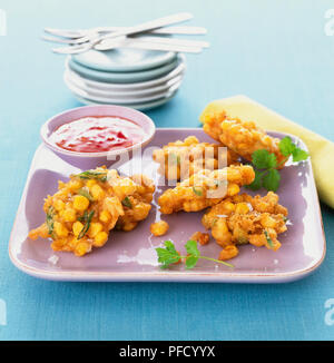 Tailandese frittelle di granturco dolce servito con salsa al peperoncino dolce sul vassoio quadrato, piastre impilate in background. Foto Stock