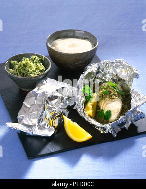 Halibut con erbe fresche e condite il riso servito in lamina di pacchi, con spicchi di limone e salsa bianca nella ciotola. Foto Stock